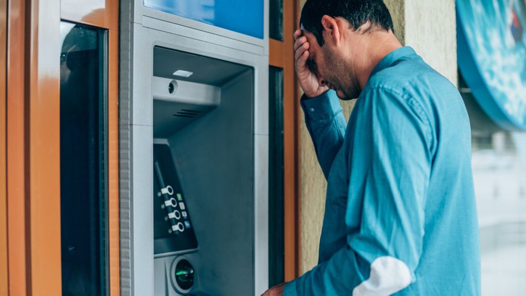 Mężczyzna przy bankomacie, łapiący się za głowę